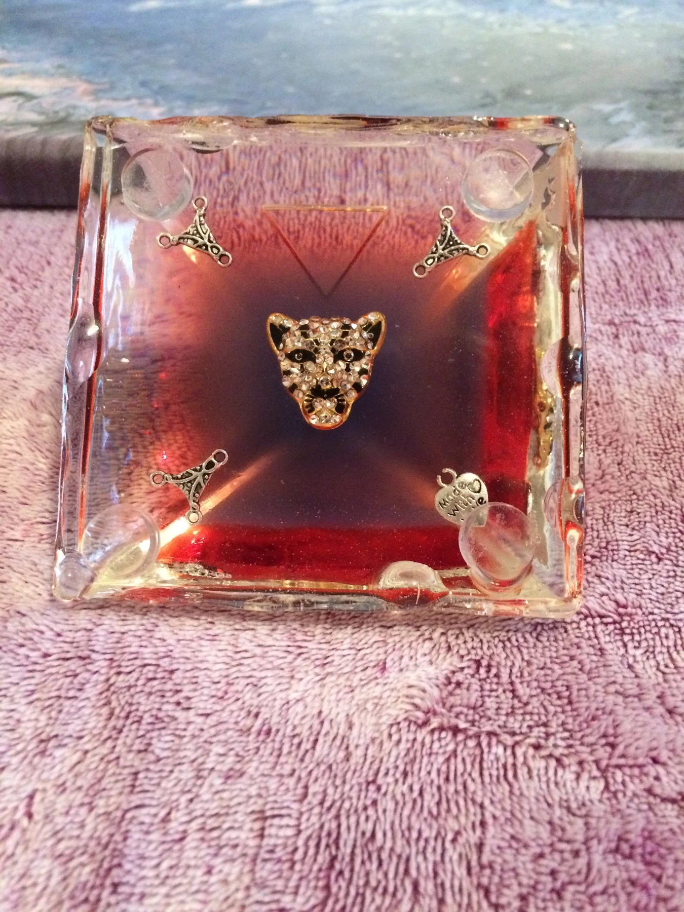 Clear red resin sculptural object with embedded metallic symbols